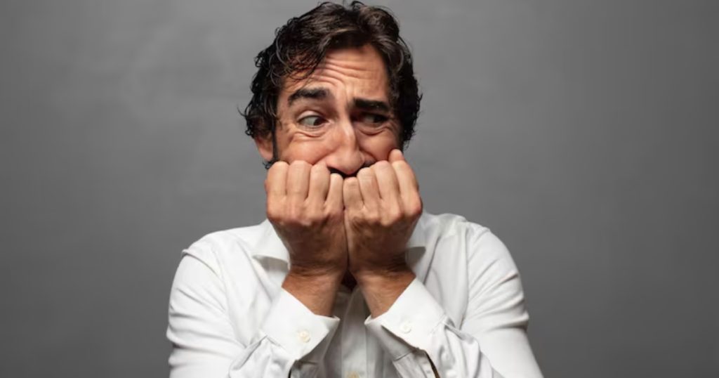 Homem adulto com as duas mãos na boca com olhar de medo