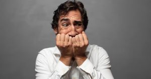 Homem adulto com as duas mãos na boca com olhar de medo