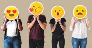 Quatro pessoas tampando os seus rostos com cartazes de carinhas redondas com diferentes emoções.