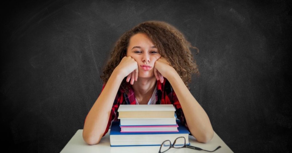 Adolescente sentada numa carteira escolar com cara emburrada.