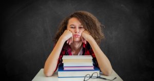 Adolescente sentada numa carteira escolar com cara emburrada.