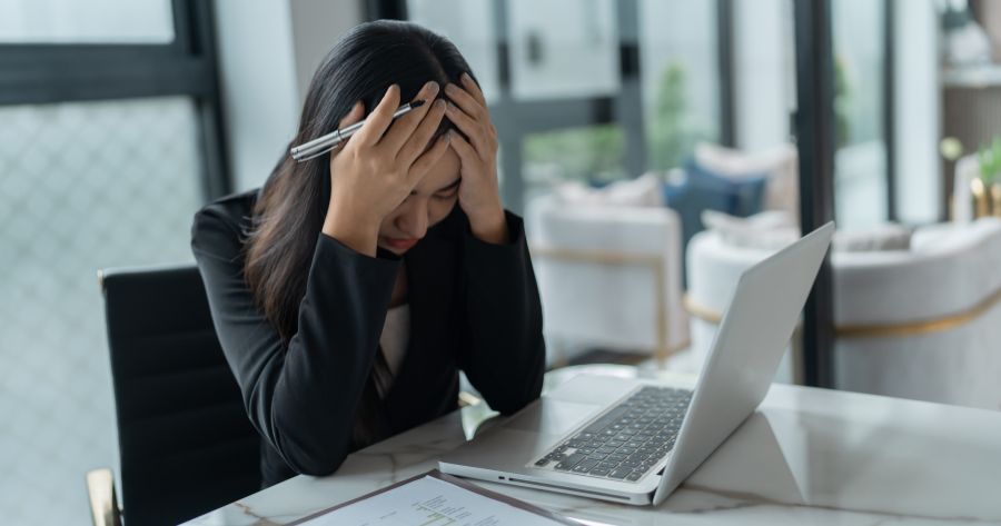 Mulher jovem morena com as mãos na cabeça estressada no trabalho.
