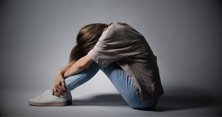 Pessoa sentada no chão com os braços cruzados sob as pernas sofrendo de depressão.