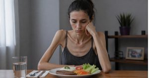 Mulher adulta magra sofrendo de transtorno alimentar olhando um prato de comida sem ânimo.