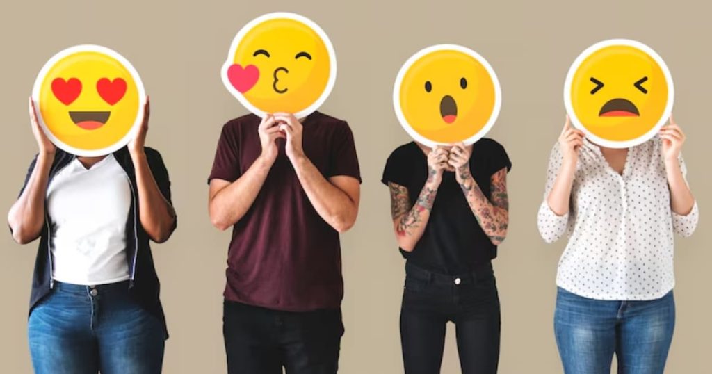 Quatro pessoas tampando os seus rostos com cartazes de carinhas redondas com diferentes emoções.